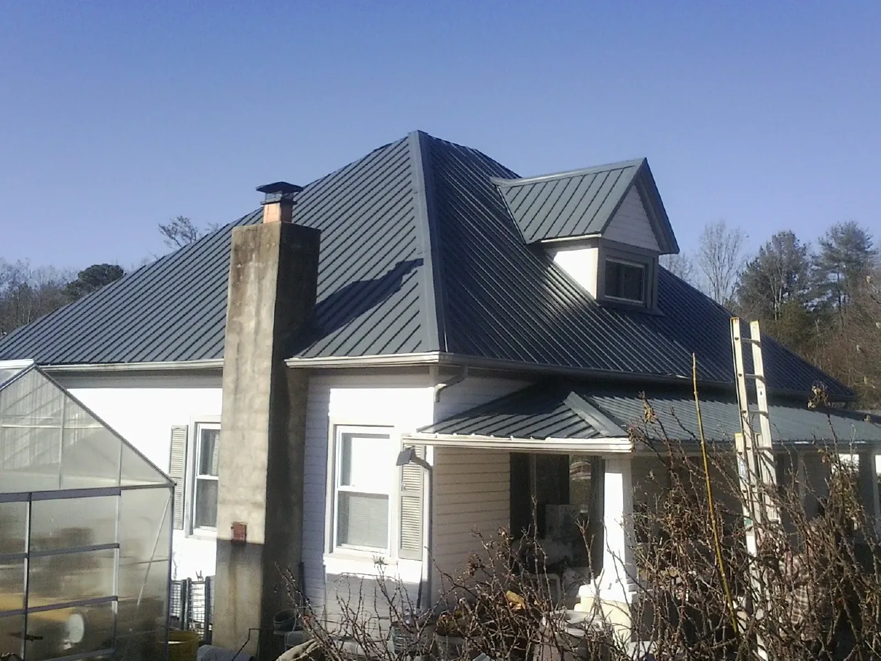 Dark blue standing seam metal roof on a white farmhouse with dormer — Slate & Tile Roof Repair by Roofing Brothers in Clint
