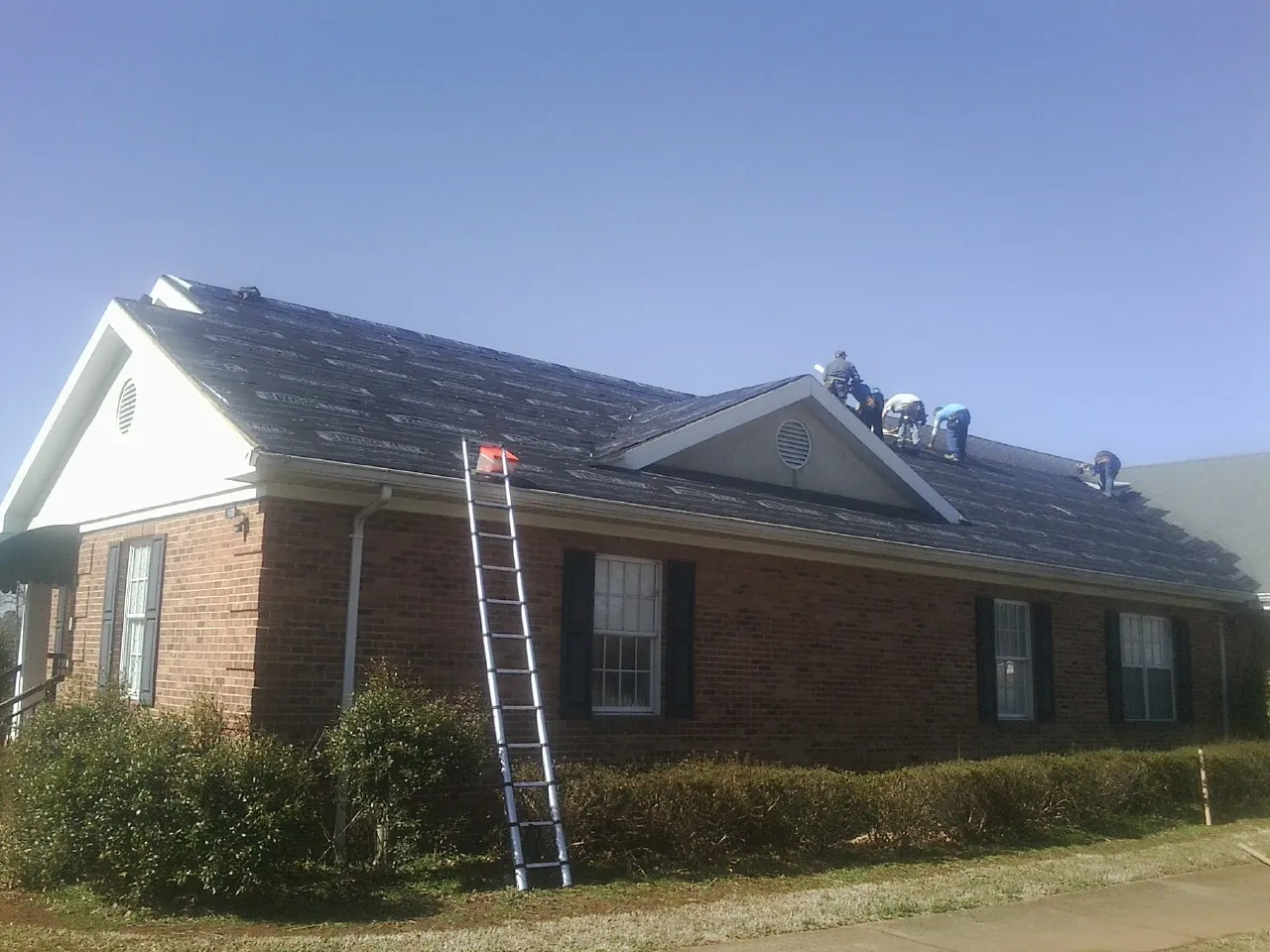 Crew tearing shingles off a brick ranch roof with a ladder set — Metal Roof Repair work by our crew in Clint