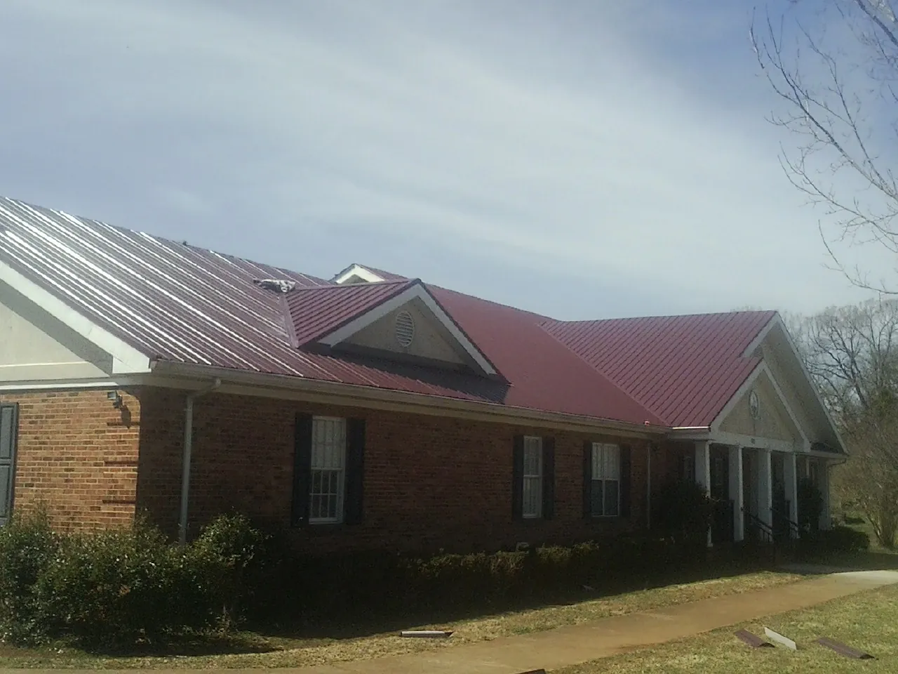 Red metal roof with gabled entries on a long brick building, from a Hail Damage Roof Repair job in Clint