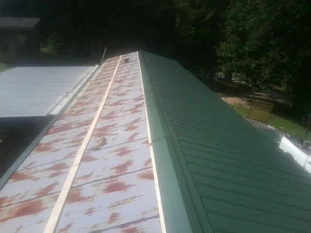 Old rusted panels beside newly installed green metal roofing — Wind Damage Roof Repair by Roofing Brothers in Clint