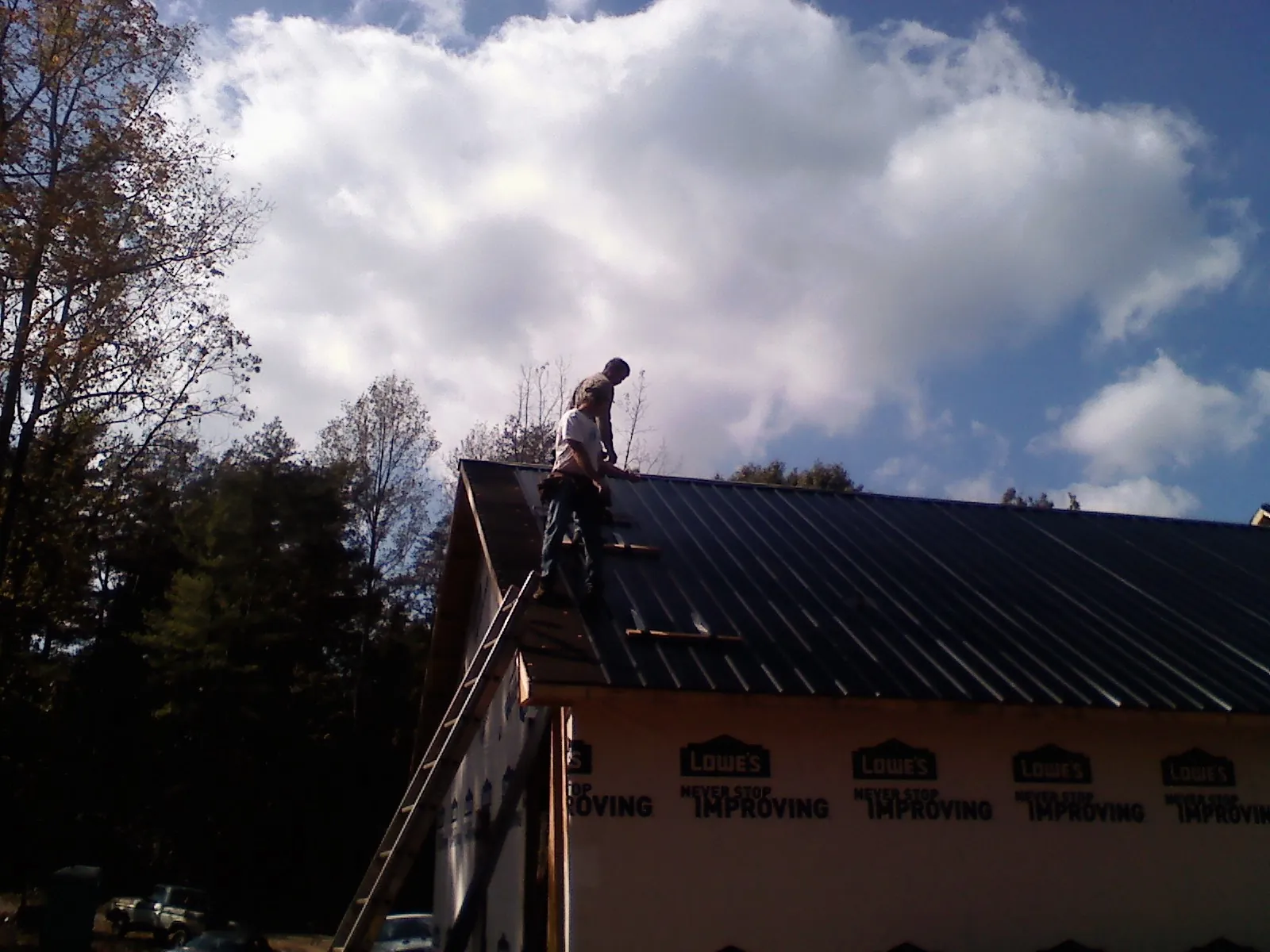 Roofer fastening dark metal panels high against a cloudy sky, from a Roof Inspection job in Clint