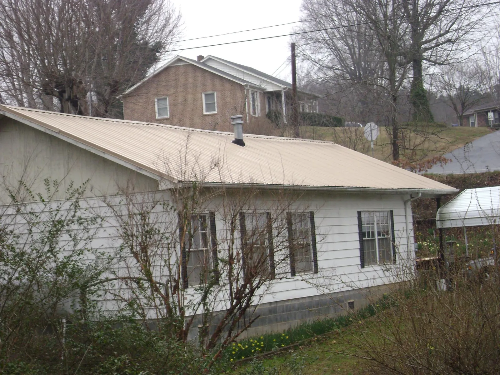 Tan metal roof on a white sided house set into a hillside — Commercial Roofing by Roofing Brothers in Clint