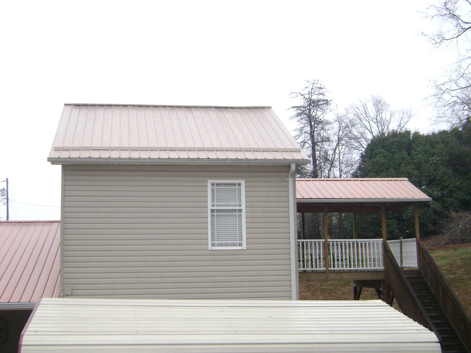 Tan metal roofs on a two story addition and attached porch, from a Roof Replacement job in Clint